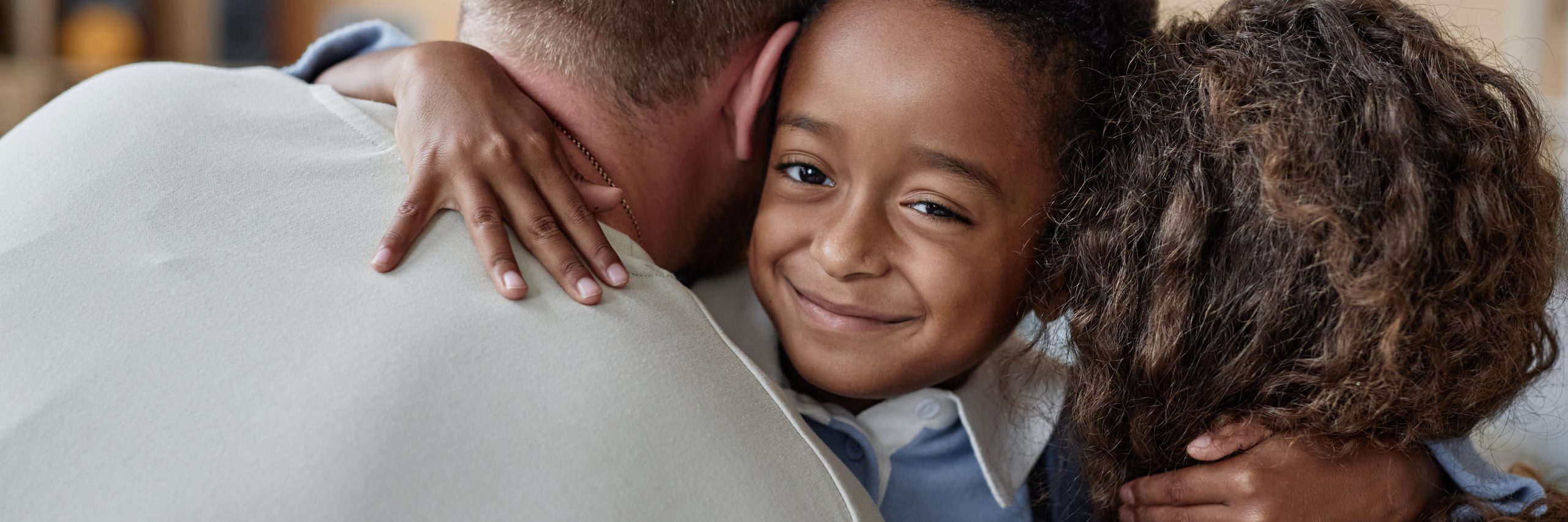 Header Image of Smiling Boy Looking at Camera while Hugging Parents