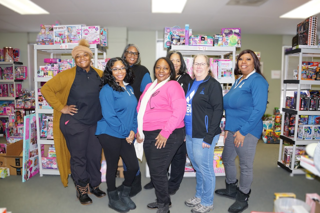 Seven women posing in front of their collection for a toy drive.